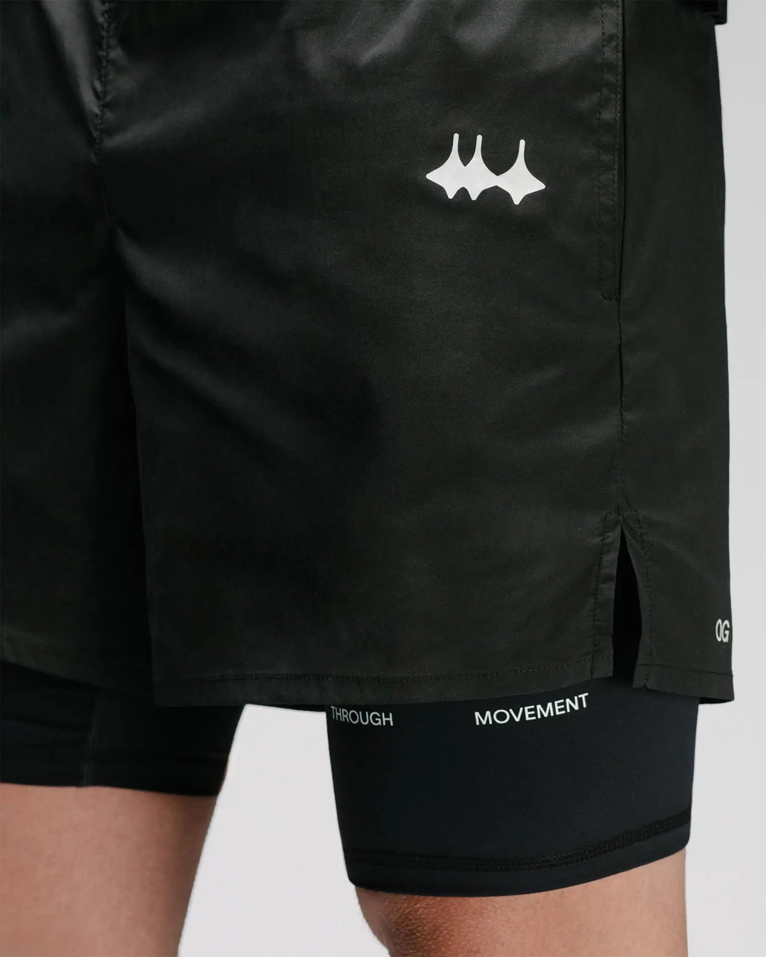 OG 01 men’s 2-in-1 shorts side detail on model — reflective logo and split hem showing inner compression layer