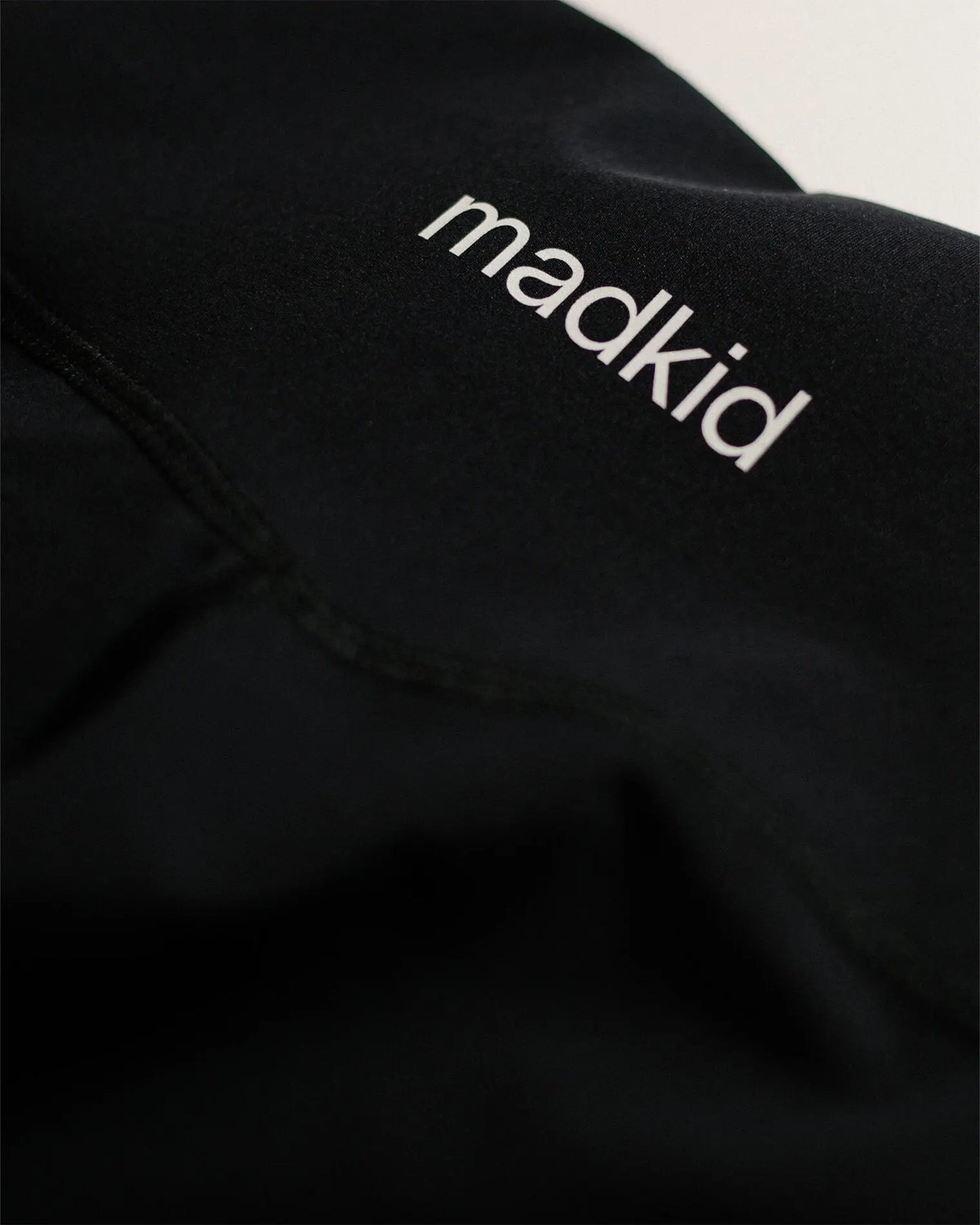 OG 01 women’s performance leggings logo detail — close-up of printed Madkid branding on black stretch fabric