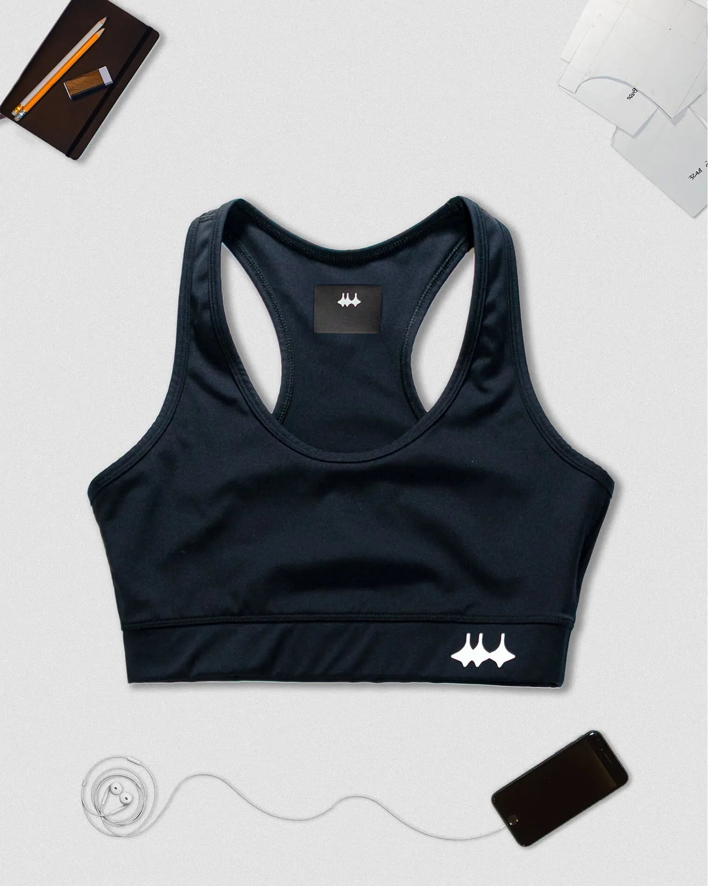 OG 01 women’s performance top front flatlay — black sports bra on light background with Madkid logo and accessories